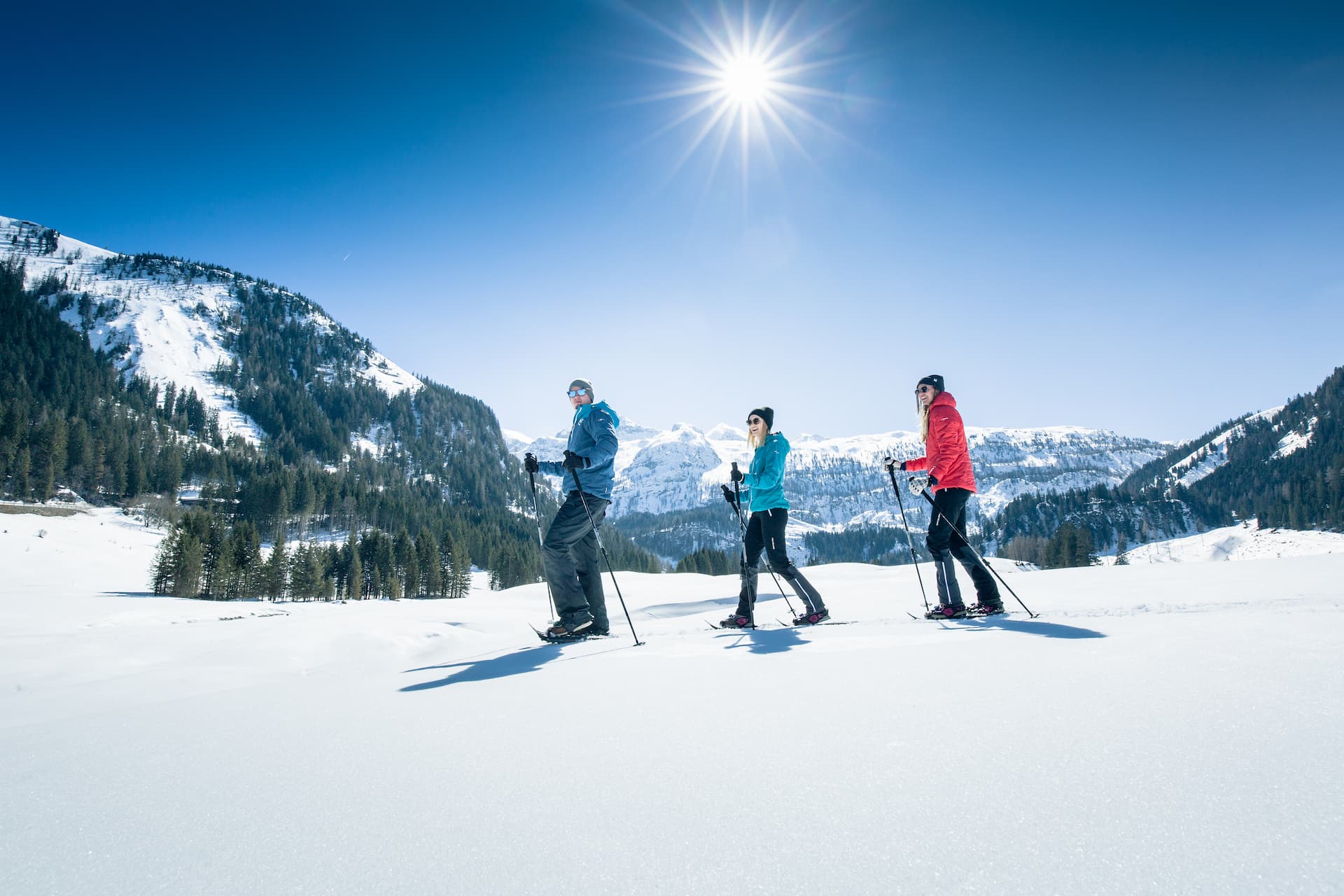 Eine Gruppe von 3 Personen genießen beim Schneeschuhwandern in Obertauern die herrliche Winterlandschaft und den strahlenden Sonnenschein im März